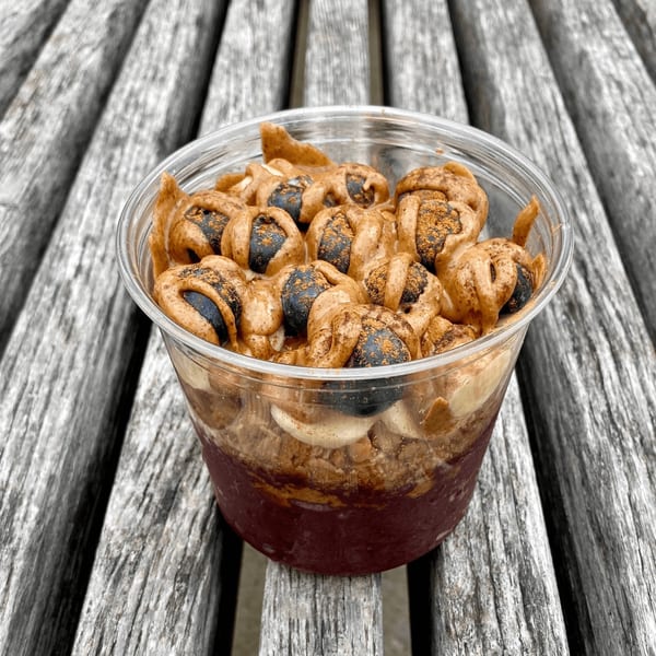 A Twenty Two Juice Bar acai bowl with blueberries and peanut butter drizzle on a wooden table.