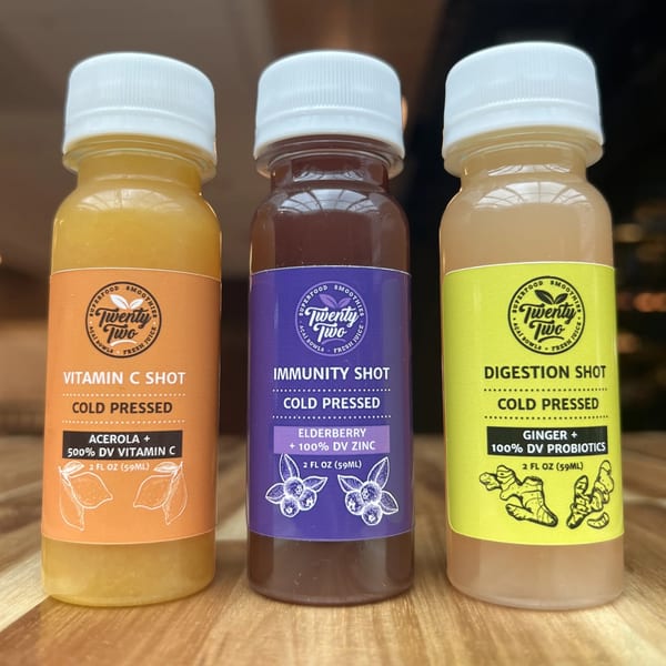 Three Twenty Two Juice Bar cold-pressed shots: Vitamin C, Immunity, and Digestion, on a wooden surface.