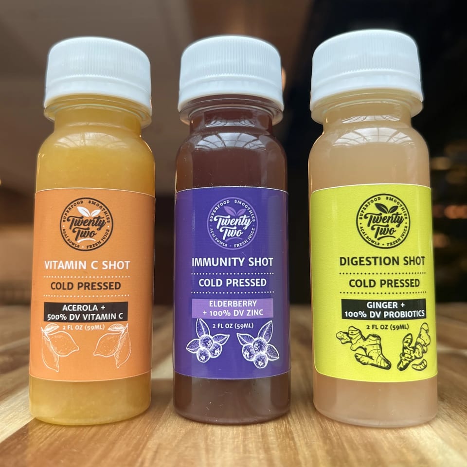 Three Twenty Two Juice Bar cold-pressed shots: Vitamin C, Immunity, and Digestion, on a wooden surface.