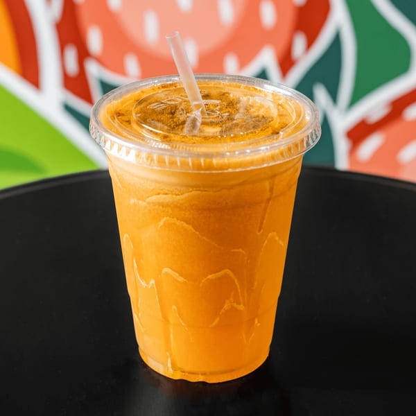 A vibrant orange juice in a clear plastic cup with a straw, on a dark table.